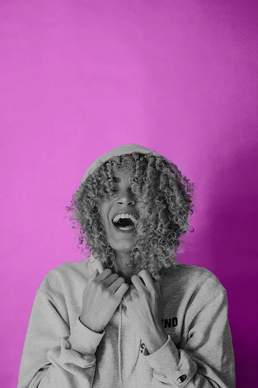 woman laughing and having fun with her hoodie over her cute curly hair against a bright, pink background, being yourself is the ultimate way to raise your vibration