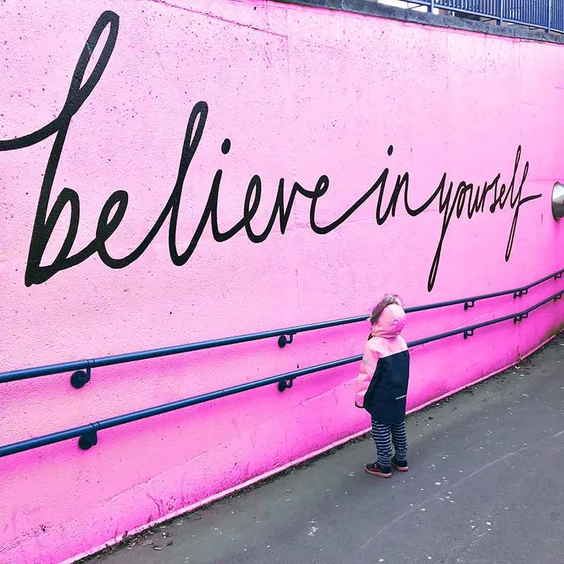 Child looking at a wall with the text believe in yourself, affirmations help with your manifestions