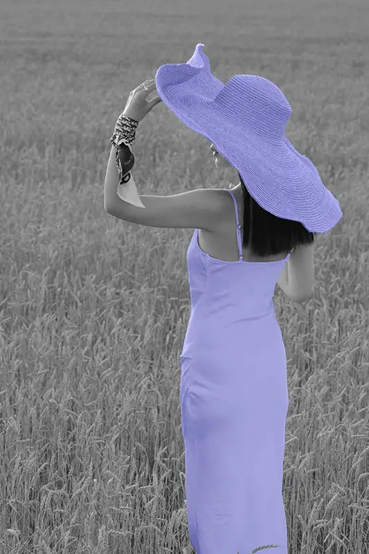 Feminine woman standing in a field wearing a silk dress and wide summer hat