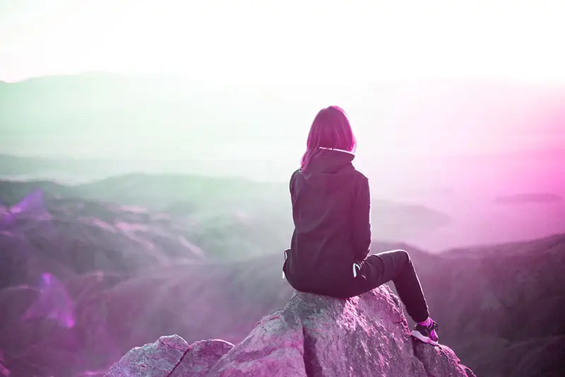 Woman sitting on top of a rock watching a beautiful view in the mountains