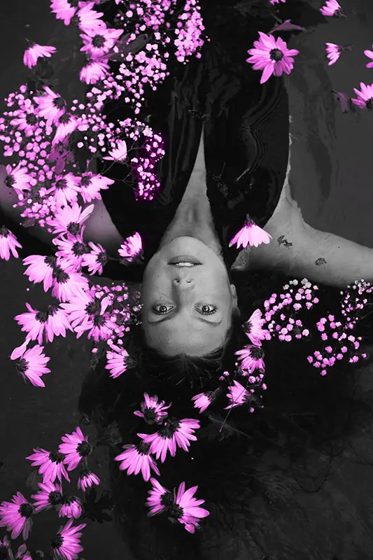 Woman floating in the water surrounded by pink flowers