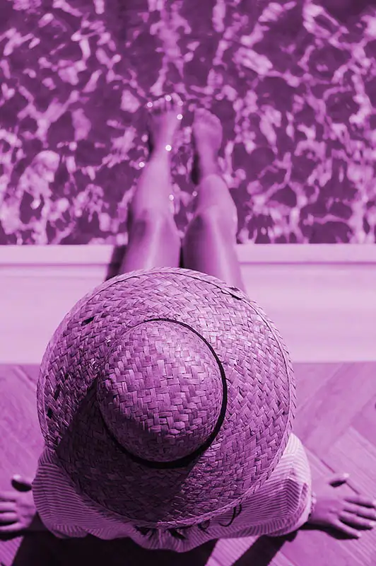 Woman with hat sunbathing next to a swimming pool, living an abundant life with the law of attraction